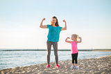 Healthy mother and baby girl showing biceps on beach