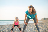 Healthy mother and baby girl workout on beach in the evening