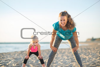 Healthy mother and baby girl workout on beach in the evening