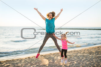 Healthy mother and baby girl jumping on beach in the evening