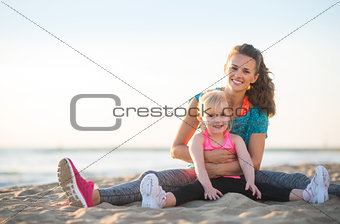 Healthy mother and baby girl sitting on beach in the evening