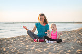 Healthy mother and baby girl doing yoga on beach in the evening