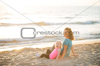 Healthy mother and baby girl sitting on beach in the evening