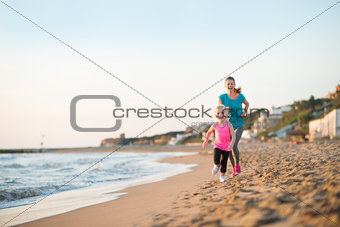 Healthy mother and baby girl running on beach in the evening