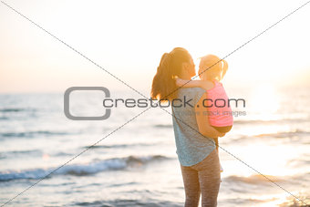 Healthy mother and baby girl looking into distance on beach in t