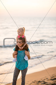 Happy baby girl sitting on shoulders of mother on beach in the e