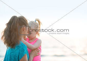 Healthy mother and baby girl hugging on beach in the evening