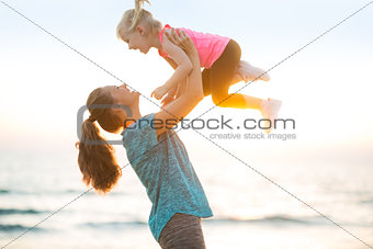 Mother throwing baby up on beach in the evening