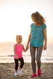 Healthy mother and baby girl walking on beach in the evening