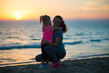 Silhouette of mother and baby girl hugging on beach