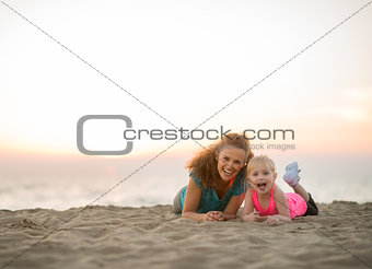 Healthy mother and baby girl laying on beach in the evening