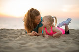 Happy mother and baby girl laying on beach in the evening