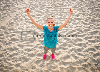Full length portrait of fitness young woman rejoicing on beach