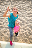 Portrait of healthy mother and baby girl on beach pointing