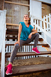 Fitness young woman sitting on stairs of beach house