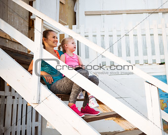 Healthy mother and baby girl sitting on stairs of beach house an