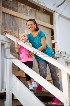 Healthy mother and baby girl standing on stairs of beach house