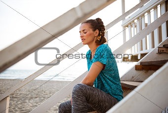 Fitness young woman sitting on stairs of beach house