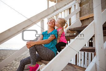 Healthy mother and baby girl kissing on stairs of beach house