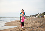 Healthy mother and baby girl running on beach
