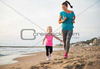 Healthy mother and baby girl running on beach