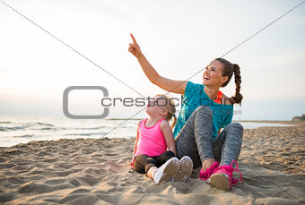 Healthy mother and baby girl sitting on beach in the evening and