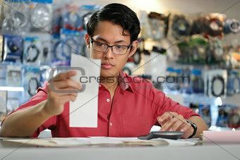 Chinese Man Working In Computer Shop Holding Bills And Invoices