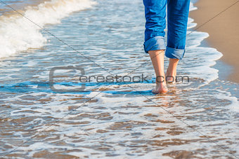male legs in jeans walking along the sandy seashore