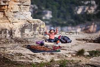 Child of rock climbers playing while sitting at the foot of a mountain next to a climbing rope