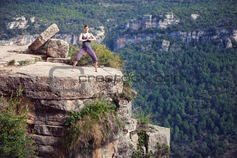 Young caucasian woman standing in yoga pose on top of cliff