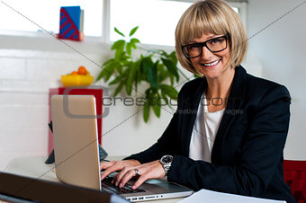 Smiling female manager typing report on laptop