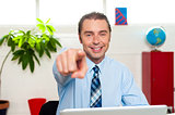 Businessman at work desk pointing at you