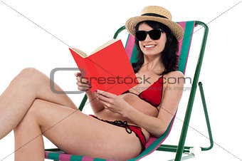 Enticing bikini model on a deckchair reading a book