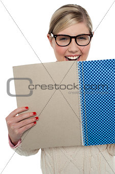 Excited teen girl holding note book close to her