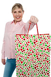 Cheerful blonde girl holding shopping bag in outstretched arm