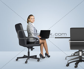 Rear view of businesslady sitting at table, holding laptop