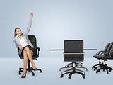 Smiling businesswoman sitting in chair and raising left hand