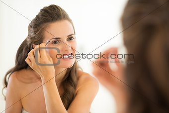 Happy young woman shaping eyebrows in bathroom
