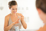Happy young woman applying nail polish in bathroom