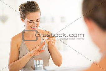 Happy young woman applying nail polish in bathroom