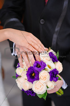 Hands of the groom and the bride on wedding bouquet