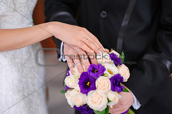 Hands of the groom and the bride on wedding bouquet