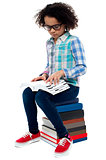 Young kid sitting on stack of books and reading