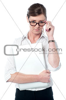 Woman looks over her glasses holding laptop
