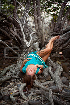 Beautiful young woman in a turquoise dress lying on roots of tree In the rainforest