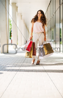 Smiling, brown-haired woman walking with colourful shopping bags