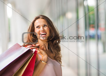 Brown-haired, happy, smiling woman holding up shopping bags