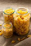 Different types of yellow macaroni pasta in glass bowl on hessian fabric cloth background