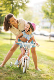 Laughing mother holding daughter on bike in a sunny city park
