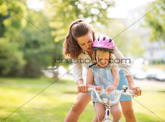 Mother shows daughter how to ride a bike holding handlebars
